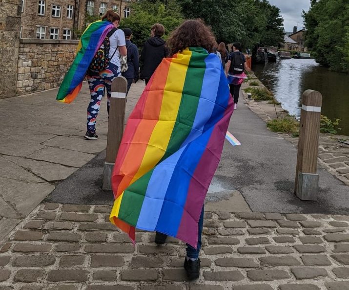 Two SELFA members walk wearing LGBTQ+ rainbow flags.